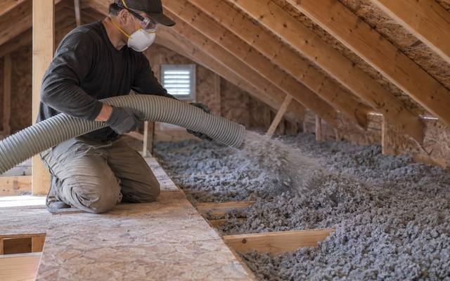 Worker blowing new loose-fill insulation along an attic walkway after insulation removal