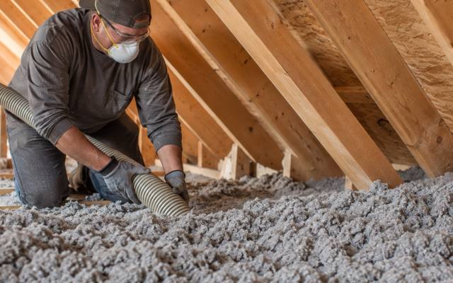 Worker holding a large hose in grey blown-in insulation under the rafters of a London attic